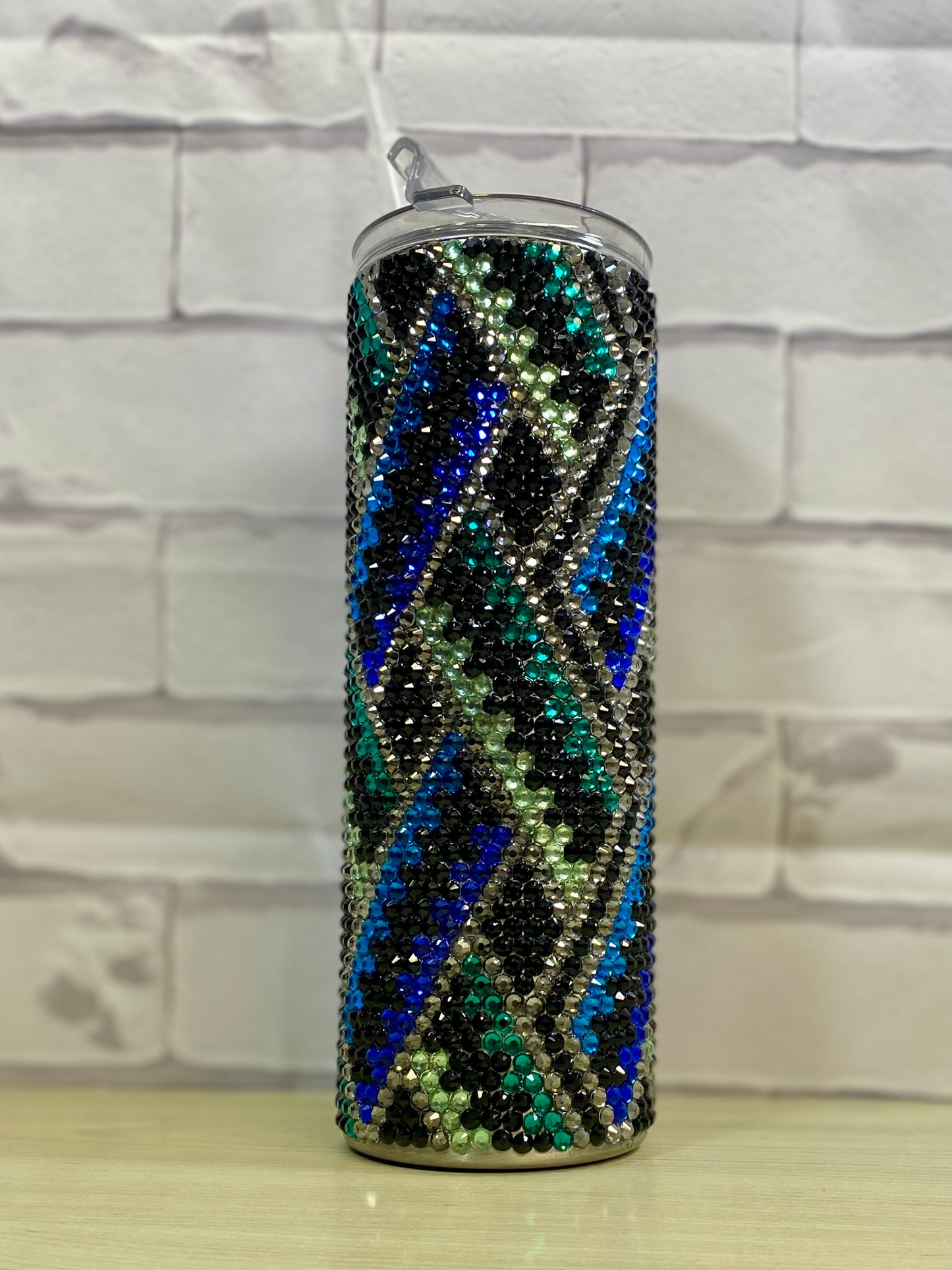 A stainless steel tumbler with a full rhinestone pattern featuring geometric blue and green lines.