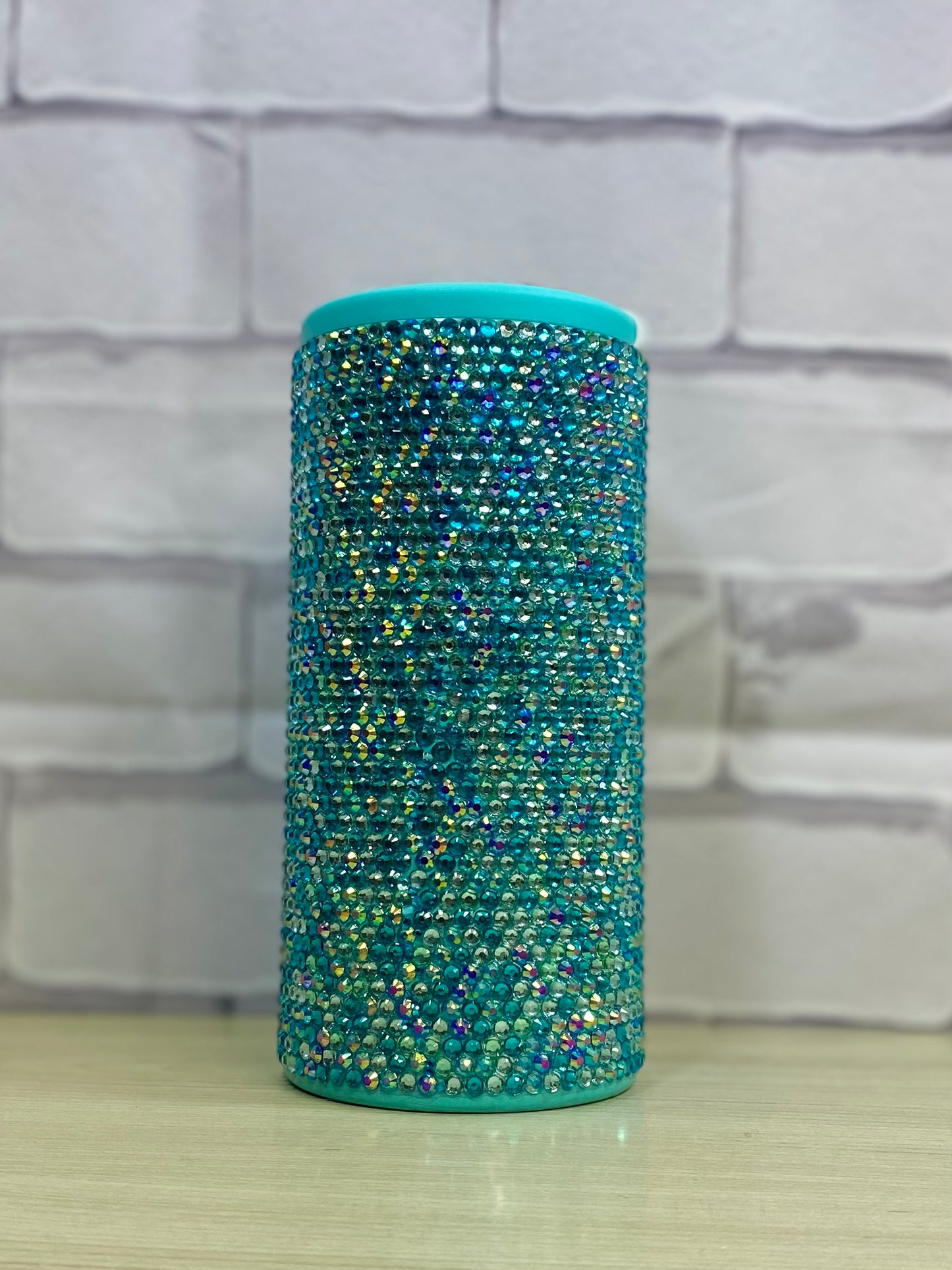 A stainless steel can cooler with a scattered rhinestone pattern in aqua tones.