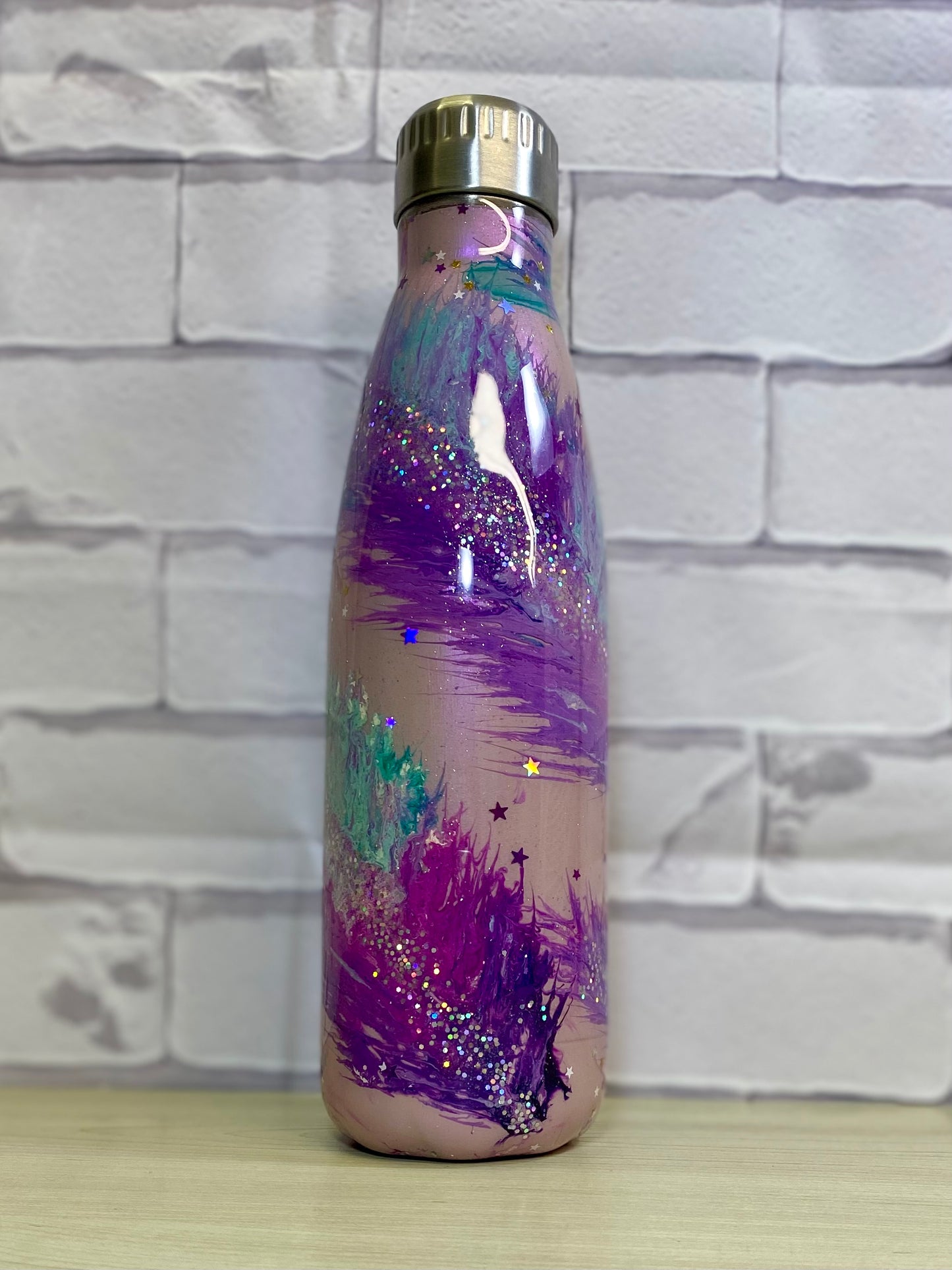 A stainless steel tumbler with a multicolored glittery design on a purple background, featuring a metallic cap.