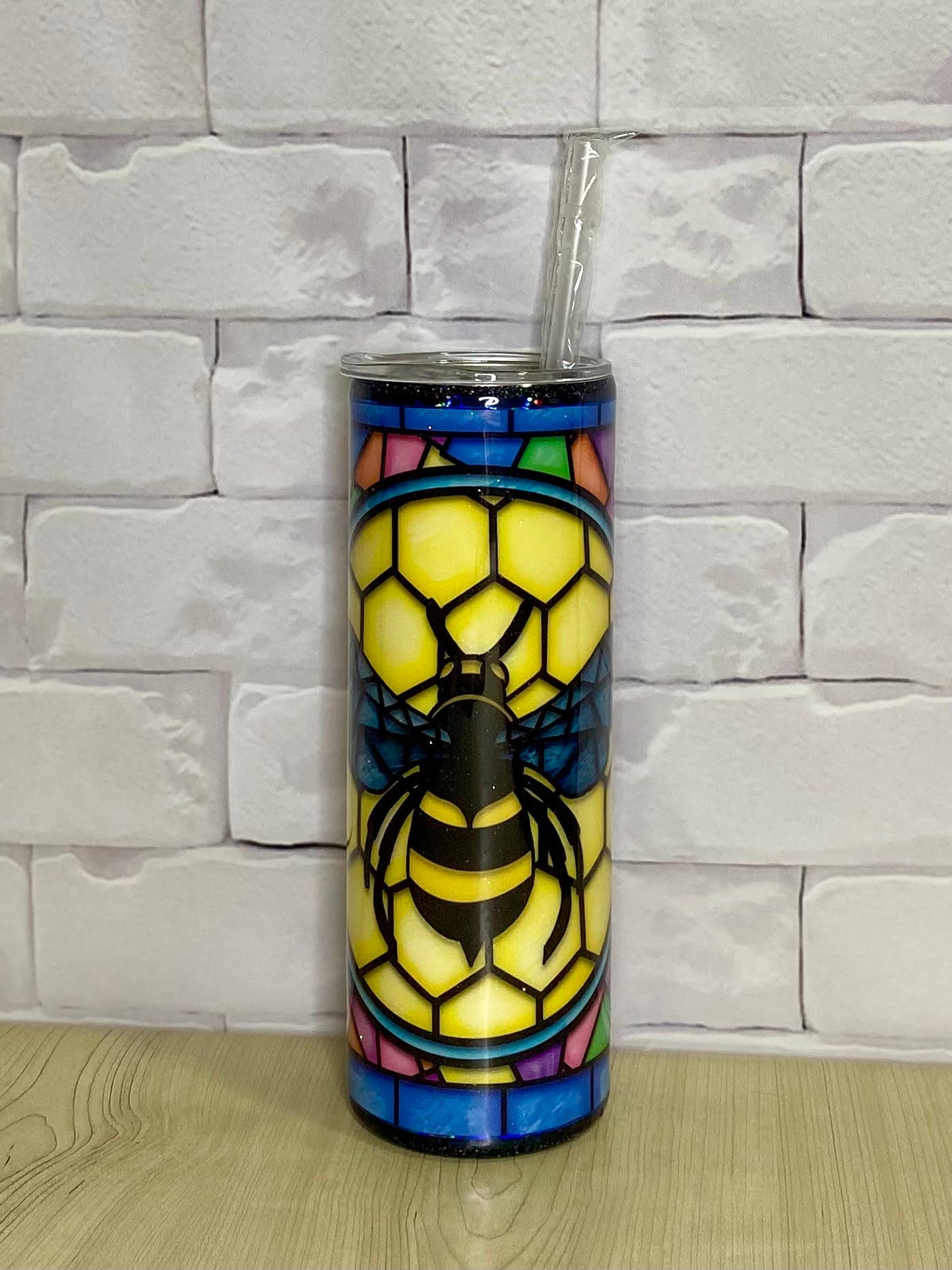 A stainless steel tumbler with a colorful geometric bee pattern on a brick wall background.