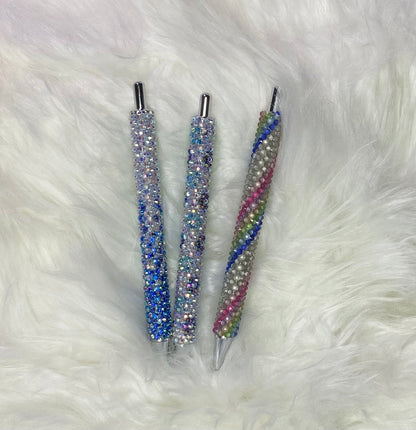Three custom order rhinestone pens with multicolored rhinestones on the barrel, lying on a white furry surface.