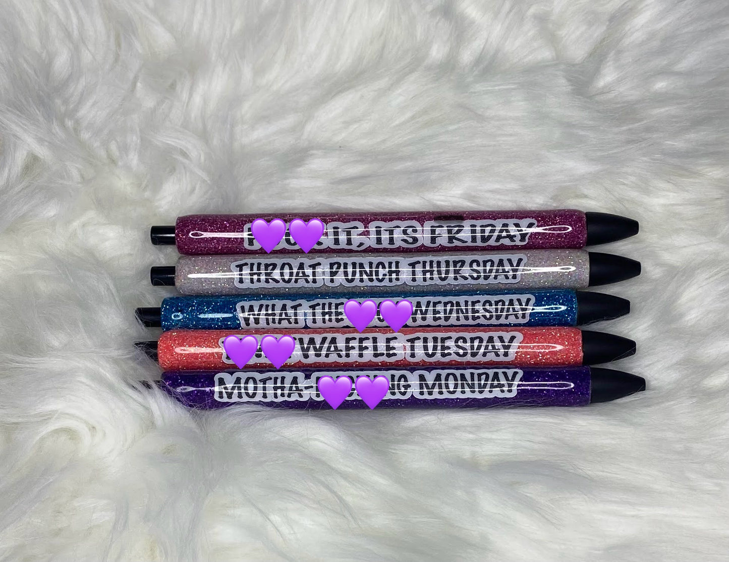 5 glittered pens with sayings on a white furry background